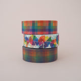 A stack of three washi tape rolls. A colourful pastel rainbow check, a dusky rainbow check, and a bright colour wheel pattern with silver-foil dots.