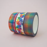Three washi tape rolls in a row. A colourful pastel rainbow check, a dusky rainbow check, and a bright colour wheel pattern with silver-foil dots.
