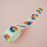 Roll of washi tape in a stamp style with perforated edges. Each stamp has a different design featuring rainbows and brightly coloured shapes.