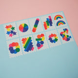 Ten stamps cut from a roll of washi tape with perforated edges. Each stamp has a different design featuring rainbows and brightly coloured shapes. They are arranged in two rows of five on a pale blue card.