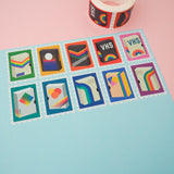 Ten stamps cut from a roll of washi tape with perforated edges. Each stamp has a different retro VHS tape design with a colourful bacground. They are arranged in two rows of five on a pale blue card.