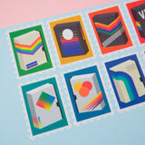 Close up of stamps cut from a roll of washi tape with perforated edges. Each stamp has a different retro VHS tape design with a colourful bacground. They are arranged in two rows on a pale blue card.