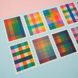 Close up of stamps cut from a roll of washi tape with perforated edges. Each stamp has a different, colourful gingham-patterned design. They are arranged in two rows on a pale blue card.