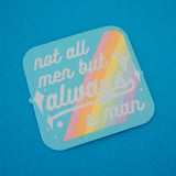 Square woven patch with rounded corners that reads not all men but always a man in white script with decorative white sparkles. The background of the patch is pale blue with pastel rainbow stripes running diagonally from top-right to bottom-left. The patch has a pale blue border.