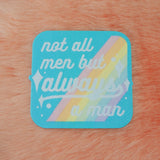 Square woven patch with rounded corners that reads not all men but always a man in white script with decorative white sparkles. The background of the patch is pale blue with pastel rainbow stripes running diagonally from top-right to bottom-left. The patch has a pale blue border.