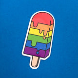 Vinyl sticker in the shape of an ice lolly. The lolly has horizontal rainbow stripes with the bright colours dripping into neighbouring sections like it is melting. The sticker has a white border.