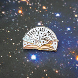 Semi-circular, lilac pin with the words Books Are Magic in capital letters. There is an open book at the bottom and many magical items are bursting forth from the pages, including a wand, raven skull, quill, stars and bubbles. The pin is on a background of stars.
