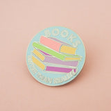 Light blue, circular enamel pin showing a stack of pastel-coloured books in the centre. Around the edge are the words Books Better Than Reality in white capital letters. The pin is on a light pink background.