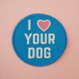 Round embroidered patch that reads I heart Your Dog in white capitals. The background is blue and the heart is pastel pink. The patch has blue merrowed edges.