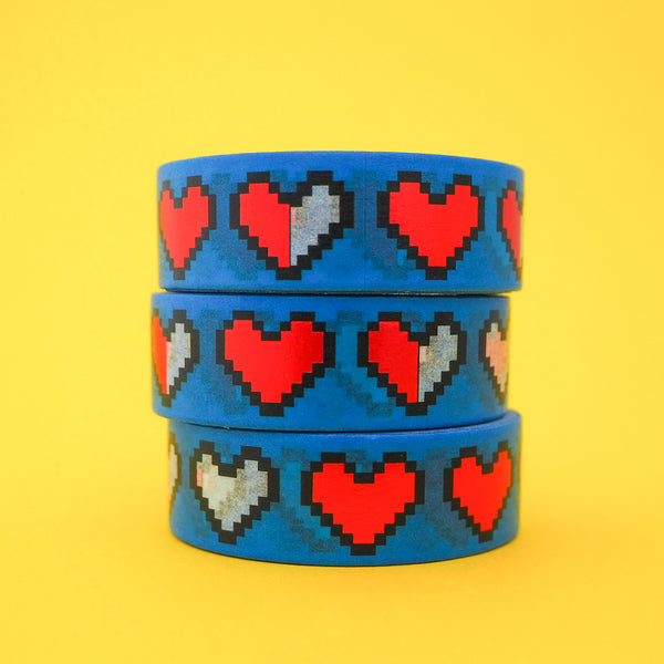Stack of blue washi tape with pixelated hearts. The hearts are outlined in black and filled with red-foil. Some hearts are half red-foil and white print or just white print.