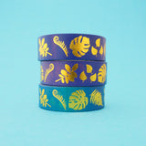 Stack of purple and blue gradient washi tape with a variety of gold-foil plants and leaves.