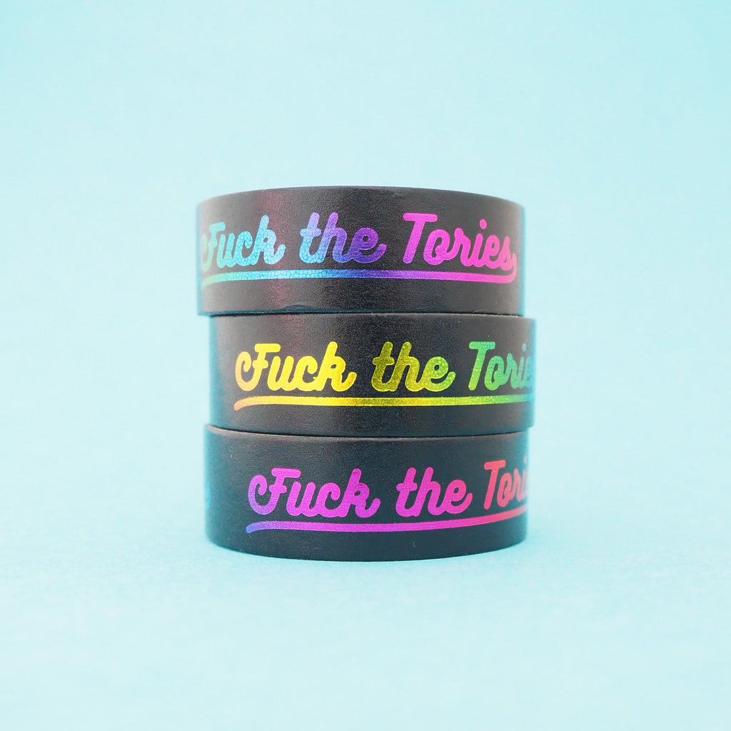 A stack of black washi tape that reads Fuck the Tories in a gradient rainbow foil.