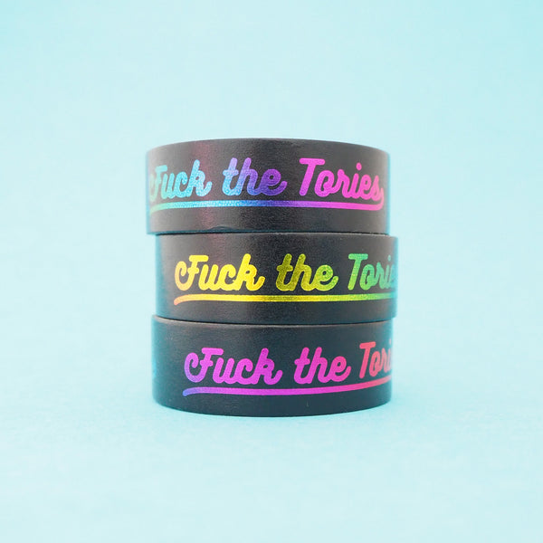 A stack of black washi tape that reads Fuck the Tories in a gradient rainbow foil.