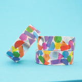 Stack of white washi tape with a scattered design of colourful shapes. The colours change where the shapes overlap. Accented with silver foil shapes.