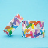 Stack of white washi tape with a scattered design of colourful rectangles. The colours change where the rectangles overlap. Accented with silver foil rectangles.
