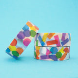 Stack of three white washi tape with a scattered design of colourful shapes. One has circles, one has rectangles. and the third has a variety of shapes. The colours change where the shapes overlap. Accented with silver foil.