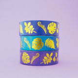Stack of purple and blue gradient washi tape with a variety of gold-foil plants and leaves.