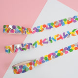 Three rolls of white washi tape with a scattered design of colourful shapes. One has circles, one has rectangles. and the third has a variety of shapes. The colours change where the shapes overlap. Accented with silver foil.