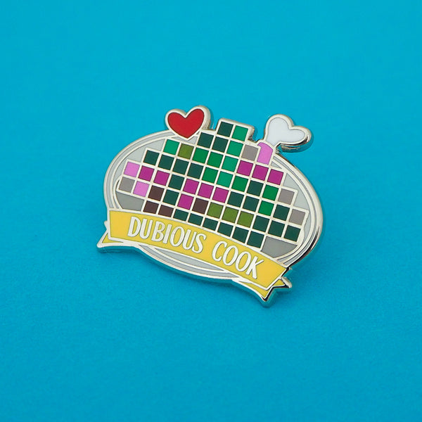 Enamel pin depicting a pixelated image on a plate with a red heart and bone protruding. A banner on the bottom reads Dubious Cook. The pin is on a blue background.