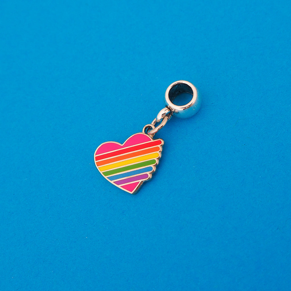 Enamel charm on a smooth cup bail bead. Charm is heart-shaped and pink with horizontal rainbow stripes. The stripes extend slightly beyond the heart on the right with rounded edges.
