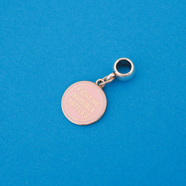 Enamel charm on a smooth cup bail bead. Charm is round and pastel pink. It bears the words Fighting Invisible Battles in silver capitals.