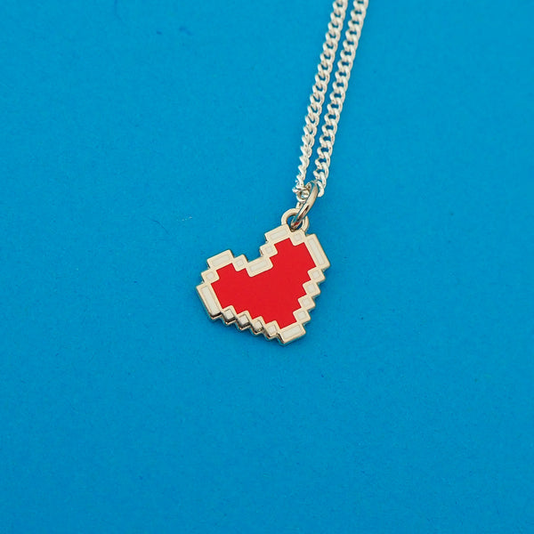Silver-plated curb chain necklace with an enamel charm pendant. Charm depicts a red, pixelated heart with a white outline.