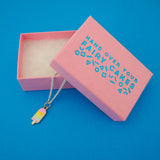 Silver-plated curb chain necklace with an enamel charm pendant. Charm is in the shape of an ice lolly. The lolly has horizontal rainbow stripes with the pastel colours dripping into neighbouring sections like it is melting. Necklace is shown emerging from a pink branded box.