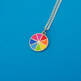 Silver curb-chain necklace with an enamel charm pendant. Charm is circular and split into eight sections. Each section is filled with a bright rainbow colour, replicating a colour wheel.