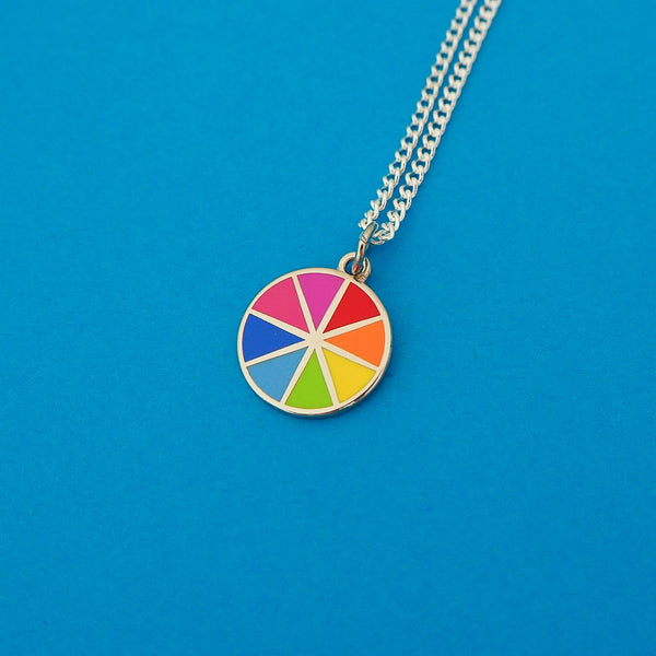 Silver curb-chain necklace with an enamel charm pendant. Charm is circular and split into eight sections. Each section is filled with a bright rainbow colour, replicating a colour wheel.