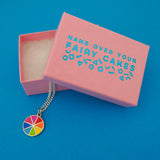 Silver curb-chain necklace with an enamel charm pendant. Charm is circular and split into eight sections. Each section is filled with a bright rainbow colour, replicating a colour wheel. Necklace is shown emerging from a pink branded box.