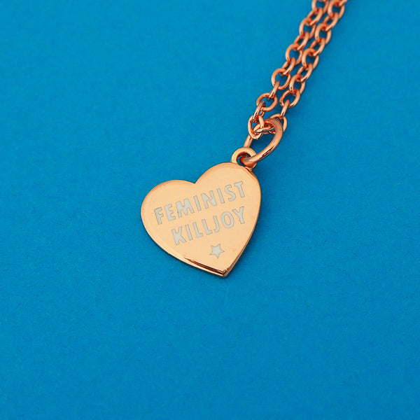 Rose-gold plated curb chain necklace with a rose-gold charm pendant. Charm is heart-shaped and bears the words Feminist Killjoy in white capital letters with a small white star beneath.