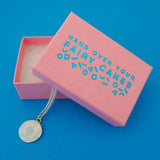 Silver curb-chain necklace with an enamel charm pendant. Charm is circular and depicts a blue, multi-faceted gem. Necklace is shown emerging from a pink branded box.