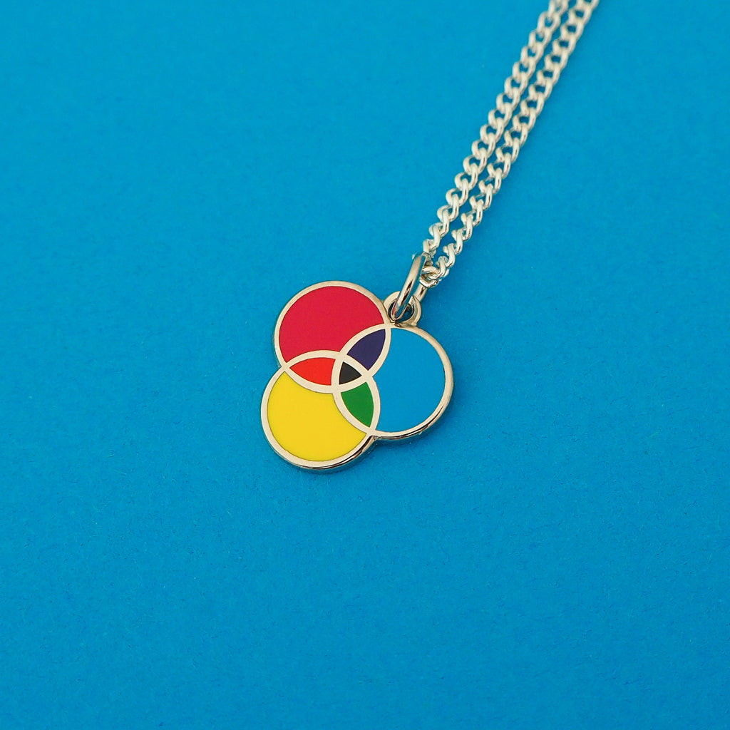 Silver curb-chain necklace with an enamel charm pendant. Charm has three overlapping circles. The circles are filled cyan, magenta, and yellow enamel, with the colours mixing in the areas where they overlap.