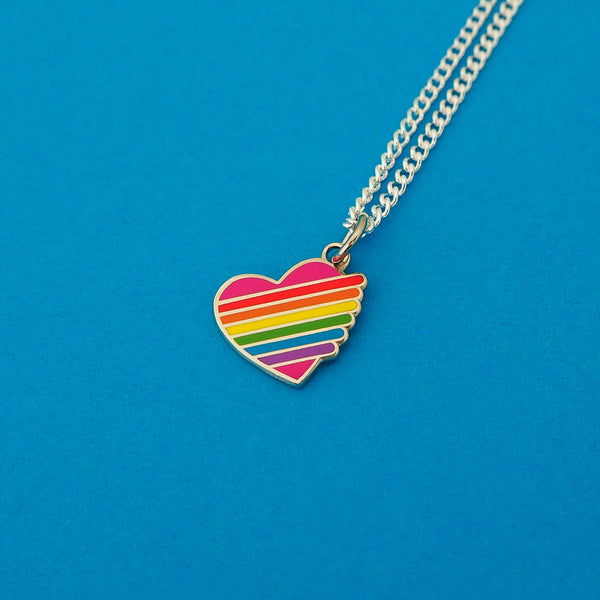 Silver-plated curb chain necklace with an enamel charm pendant. Charm is heart-shaped and pink with horizontal rainbow stripes. The stripes extend slightly beyond the heart on the right with rounded edges.
