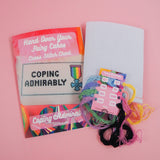 Contents of a cross stitch kit. Pack includes aida cut to size, a card with multicoloured threads and a needle, plus a pattern guide for the Coping Admirably Design.
