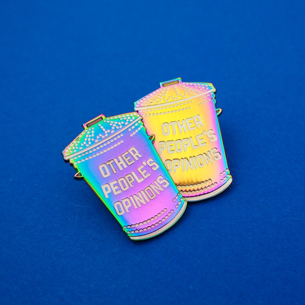 Two rainbow-plated metal pins in the shape of a rubbish bin which reads Other People's Opinions in white capitals.