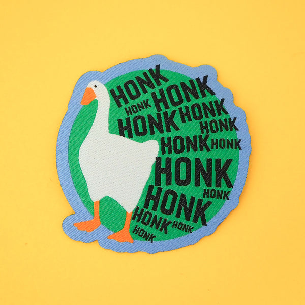 Green, circular woven patch. On the left is a goose and the rest of the patch is filled with the word Honk repeated in different sizes in black capitals. The goose and letters protrude over the edge of the circle. The patch has a blue border.