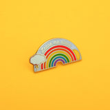 Metal pin showing a rainbow with sun and lightning cloud that reads Leave Me Alone in silver script.