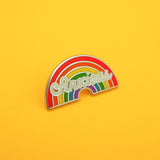 An enamel pin depicting a rainbow with the word Anxious in white script. The pin is on a yellow background.
