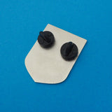 The back of a shield-shaped enamel pin with two black rubber backings. Pin is on a deep blue background.