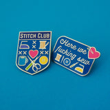 Two pins on a blue background. The first is a bright blue, shield-shaped pin with the words Stitch Club at the top in capital letters in a dark blue banner. The heart of the shield contains many images of brightly coloured sewing paraphernalia including a button, needle and thread, scissors and seam-ripper. The second is a blue rectangle with rounded corners reading Here We Fucking Sew. It also features the colourful sewing items and a large pink heart stuck with two glass-head pins.