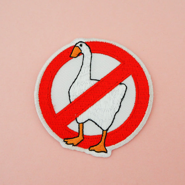 Embroidered patch showing a white goose inside a red circle with a 45-degree diagonal line from upper-right to lower-left, mimicking a prohibition sign. The patch has white merrowed edges.