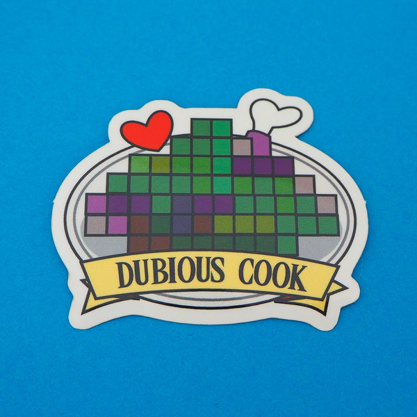 Vinyl sticker depicting a pixelated image on a plate with a red heart and bone protruding. A banner on the bottom reads Dubious Cook. The sticker has a white border.