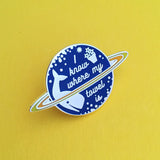 Pin in the shape of a ringed planet. The globe is deep blue and the 2 rings are shades of yellow. On the globe is whale, a flower pot, and the words I know where my towel is in silver script. The pin is on a yellow background.