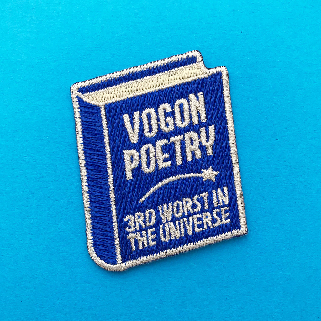 Deep blue embroidered patch shaped like a book. The cover reads Vogon Poetry 3rd Worst in the Universe in silver capitals with a shooting star in the centre. The patch has silver merrowed edges.