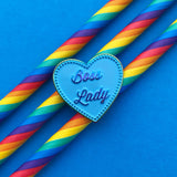 Heart-shaped metal pin filled with light blue enamel. In the centre of the heart are the words Boss Lady in rainbow-plated metal. The heart is outlined with a row of tiny rainbow-plated squares.