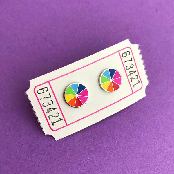 Round stud earrings, split into eight sections. Each section is filled with a bright rainbow colour, replicating a colour wheel. Earrings are displayed on a carnival ticket.