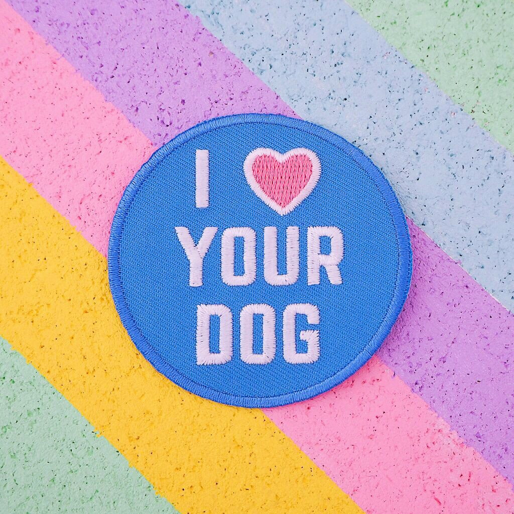 Round embroidered patch that reads I heart Your Dog in white capitals. The background is blue and the heart is pastel pink. The patch has blue merrowed edges.