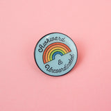 Round, light blue pin with a glitter rainbow in the centre that reads Awkward & Uncoordinated. The pin has a glossy, epoxy layer over the surface.