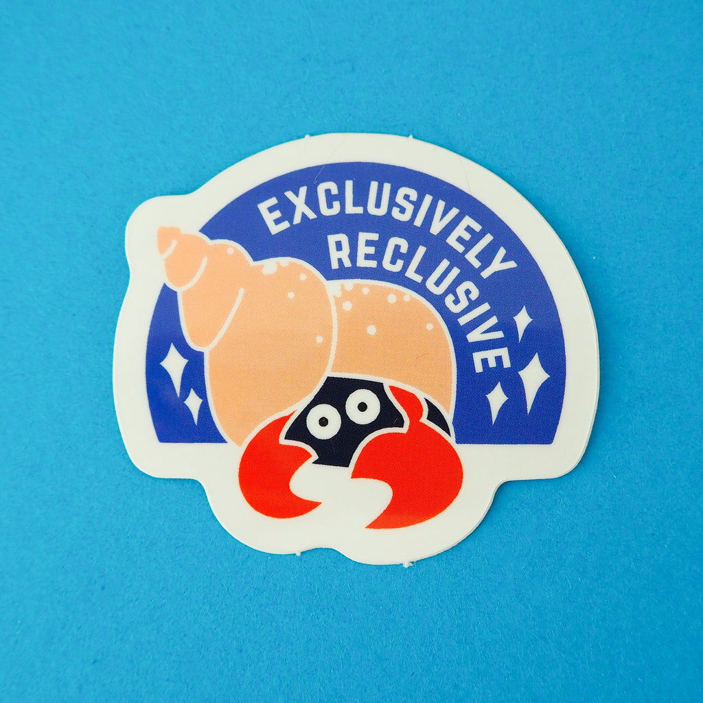 Semi-circular, blue vinyl sticker with the image of a hermit crab in a peach coloured spiral shell. Only the crabs eyes and red claws are visible, peeking out from the darkness of the shell's entrance. The words Exclusively Reclusive are written on the blue section in white capital letters with some white sparkles. The sticker has a white border.